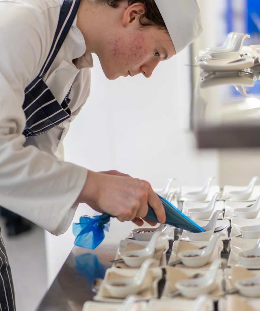 Student chef in a kitchen and chef whites preparing desserts