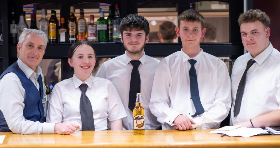 Member of HoW College staff with students stood at a bar smiling in suits