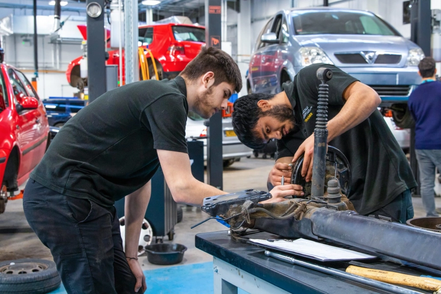 Two students working on car part in an automotive garage