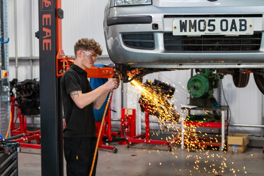 Student working on lifted car using sparking equipment