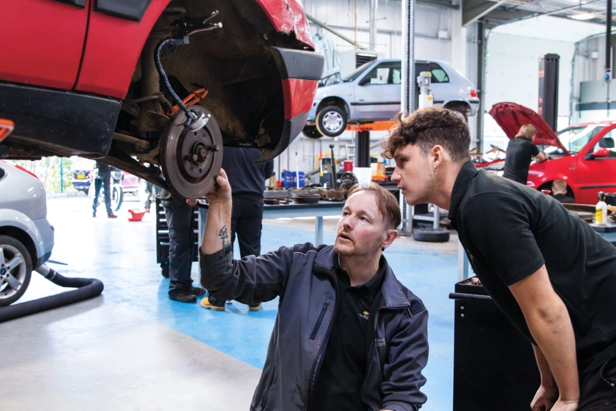 Student and teacher looking at suspended car wheel in garage