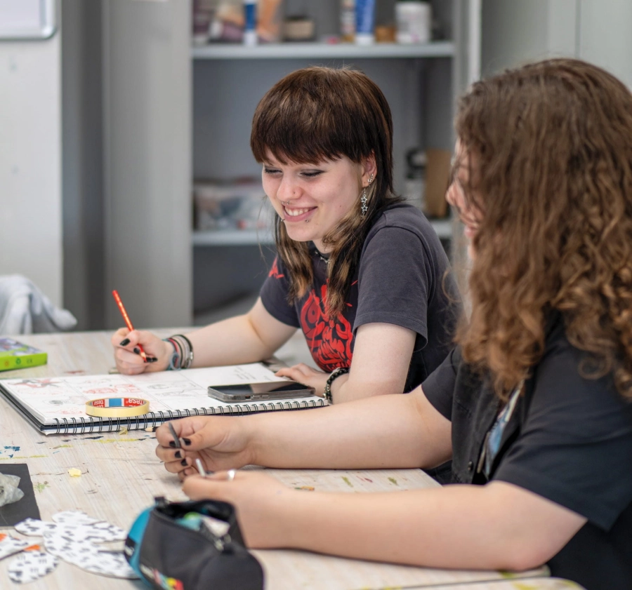 Two students sat at a desk in an art classroom drawing