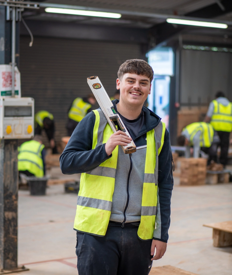 student holding a spirit level in construction workshop wearing hi vis jacket