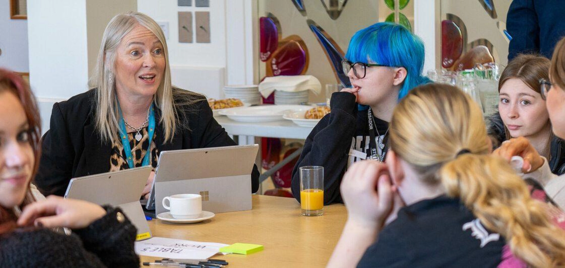 Group of students around a table speak to a staff member