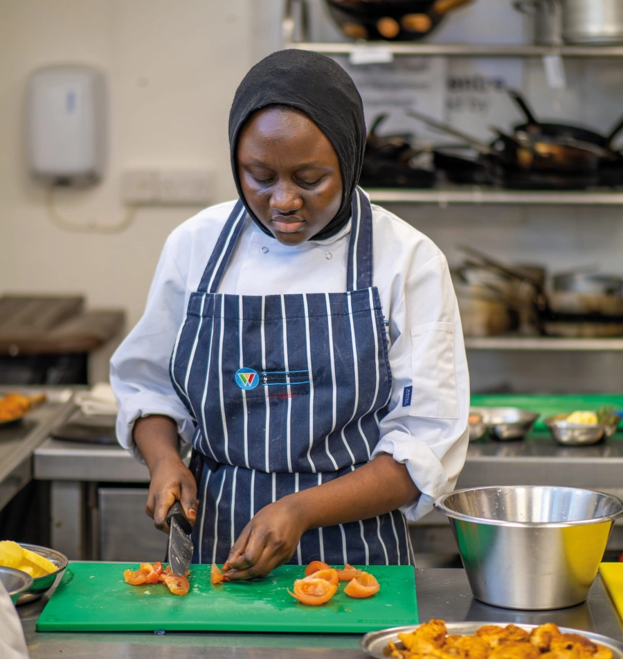 Student in a kitchen chopping vegetables