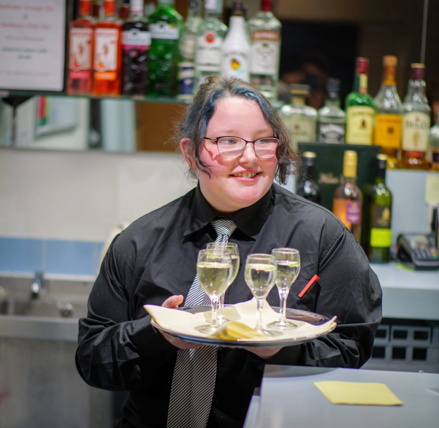Student carrying a tray with drinks on serving to guests