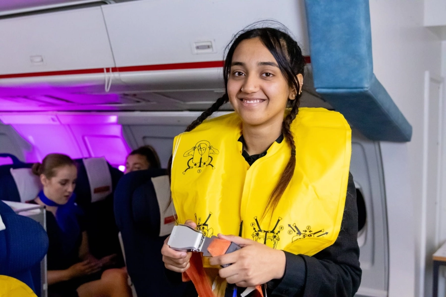 Student wearing a yellow life jacket and holding a seatbelt in mock air cabin